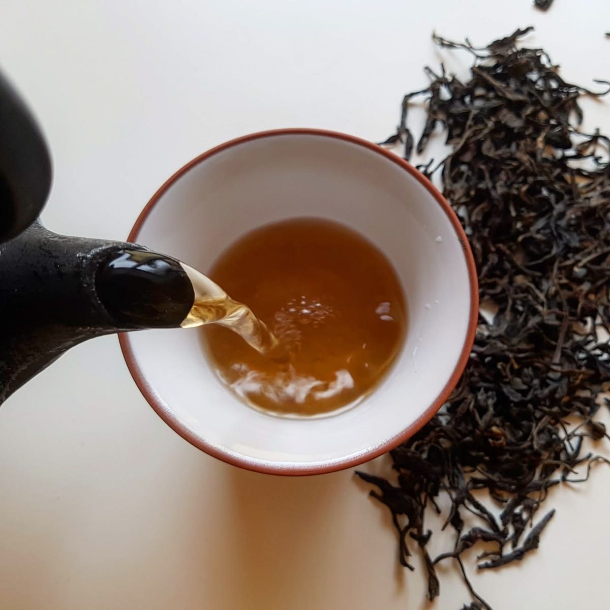 Roasted black tea being poured, with loose tea leaves beside the cup.
