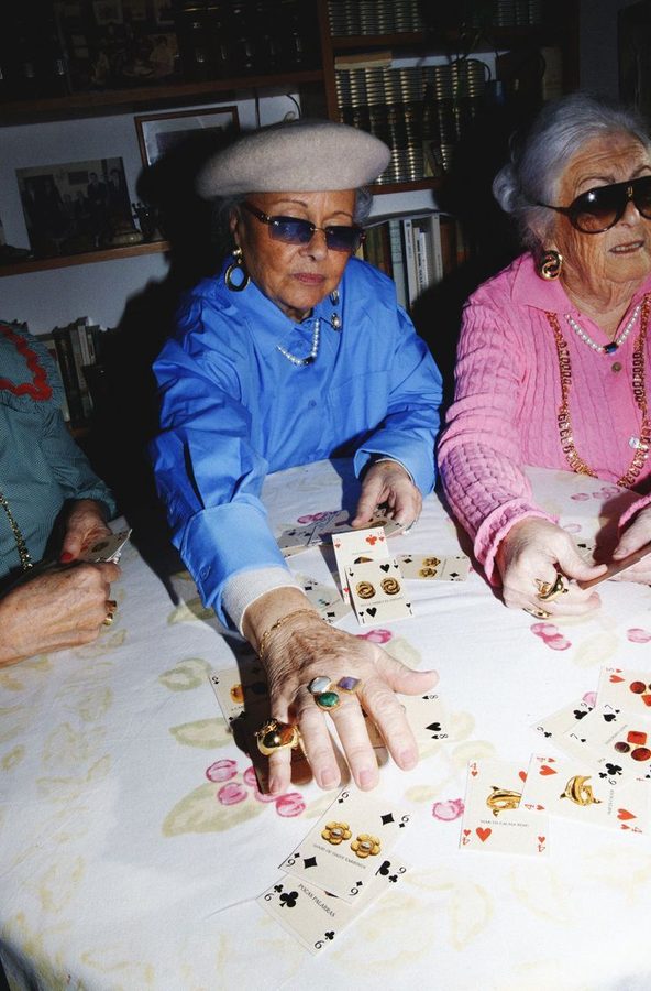 Older women wearing colorful clothing and sunglasses playing cards at a tea party.